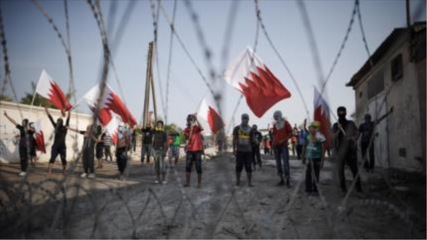 Manifestantes bareiníes ondean su bandera nacional detrás de alambre de púas colocado por la Policía en Manama (capital)
