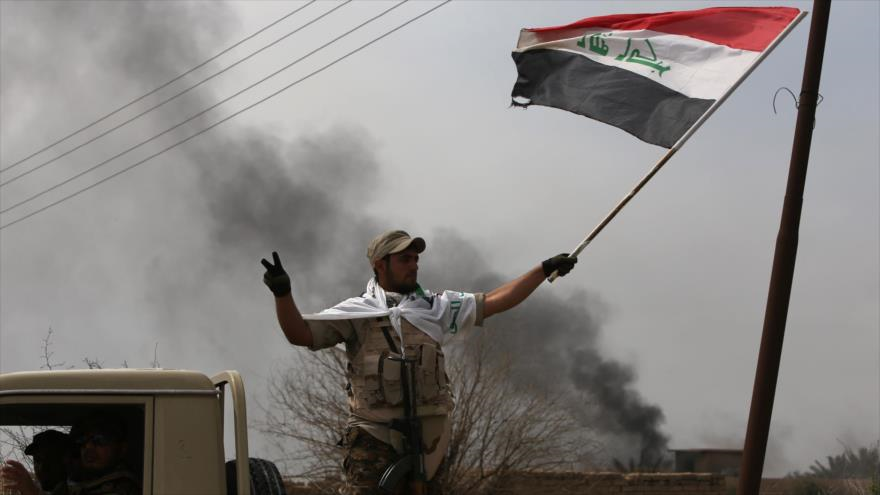 Un miembros de las fuerzas populares iraquíes ondea la bandera de Irak tras recuperación de una aldea cerca de la ciudad central de Tikrit de manos de los terroristas del EIIL