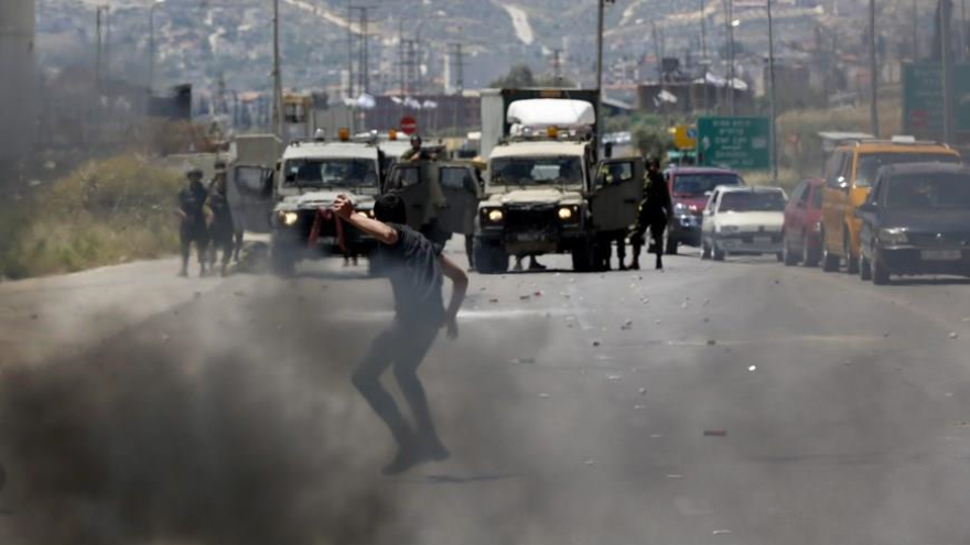 Un niño palestino arroja piedra a varios vehículos militares israelíes.