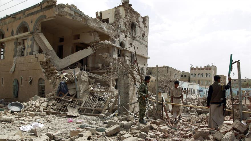 Combatientes del movimiento popular Ansarolá caminan junto a una casa destruida en un ataque saudí en Saná, capital, 3 de julio de 2015.