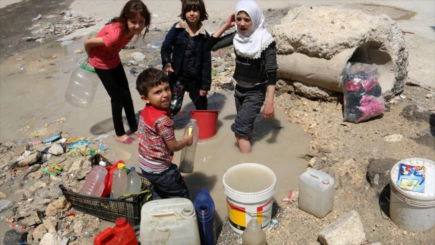 Niños sirios recogen agua al borde de un camino en la ciudad noroccidental de Alepo.