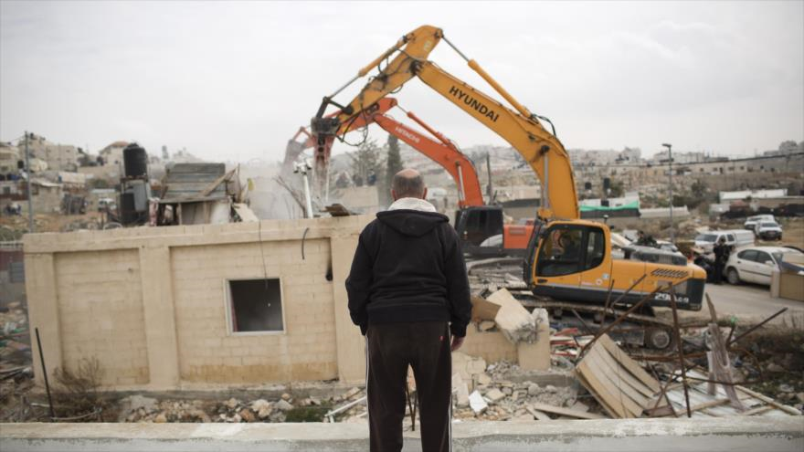 Un hombre palestino observa como las fuerzas israelíes destruyen su casa.