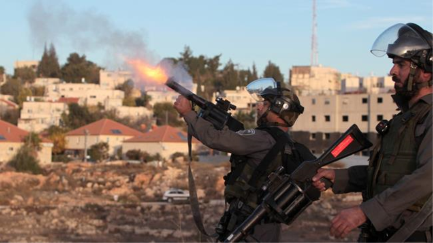 Soldado israelí dispara gas lacrimógeno contra un grupo de manifestantes palestinos.