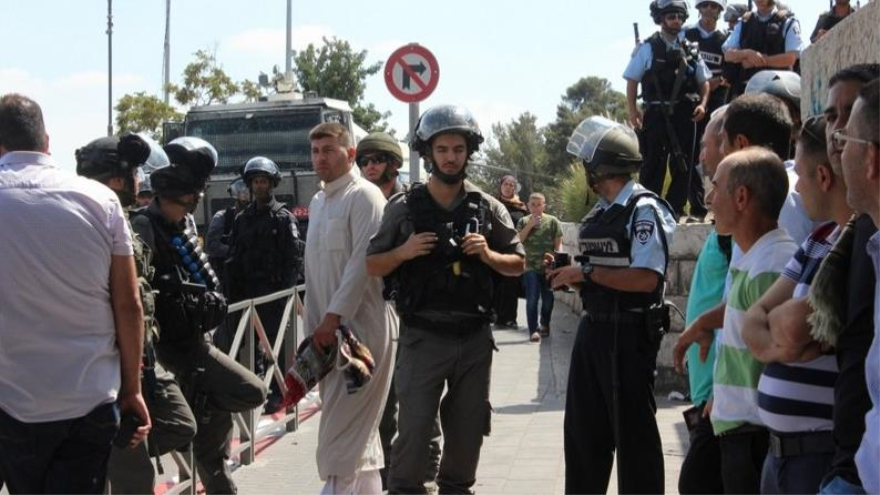 Palestinos y soldados del régimen israelí congregados en la escena del ataque en Al-Quds.