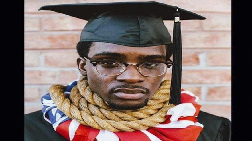 En esta foto se caracterizó como un “graduado de la universidad”, pero en todas fotografías aparece con una soga alrededor del cuello sobre una bandera estadounidense, mediante la cual quiere decir que en EE.UU. no importa cuál sea tu profesión si tienes un tono de piel más oscuro, la vida será mucho más difícil para ti.