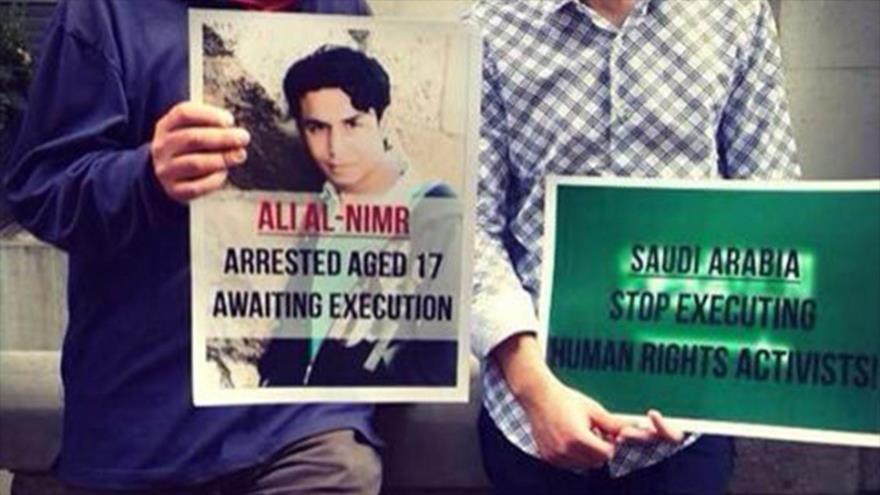 Dos personas portan pancartas; la de izquierda dice: Ali Al-Nimr, arrestado cuando tenía 17 años, esperando ejecución. La de derecha pide a Arabia Saudí poner fin a la ejecución de los activistas de derechos humanos.