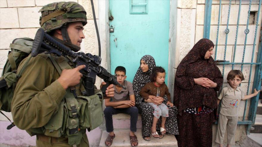 Un soldado israelí sostiene su rifle frente a una familia palestina en la localidad de Tafoh, cerca de la ciudad cisjordana de Al-Jalil (Hebrón).