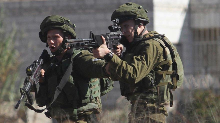 Soldado israelí apunta su arma contra palestinos en Cisjordania.