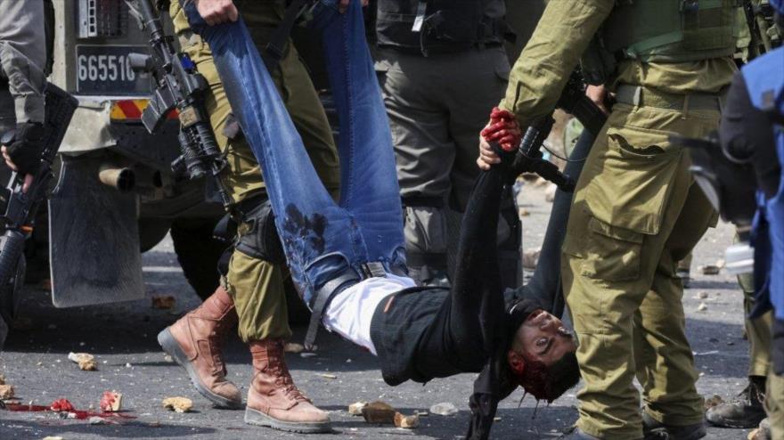 Dos soldados israelíes transportan a un palestino herido en un enfrentamiento con militares del régimen de Tel Aviv en un puesto militar cerca de la ciudad cisjordana de Ramalá.