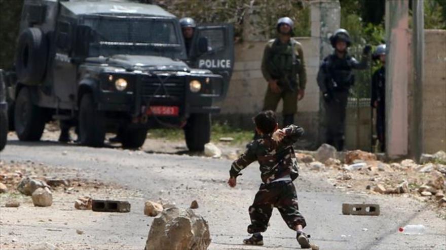 Un niño palestino arroja piedras a varios vehículos militares israelíes.