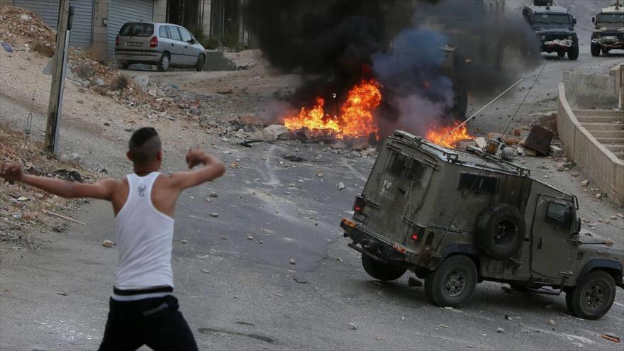 Un joven palestino arroja piedras contra los vehículos de soldados israelíes en Nablus, Cisjordania.
