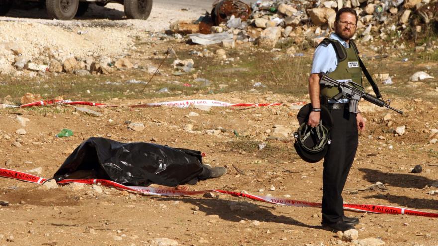 Un policía israelí vigila el cuerpo sin vida de palestino que murió por las balas de los soldados israelíes en Al-Jalil (Hebrón).