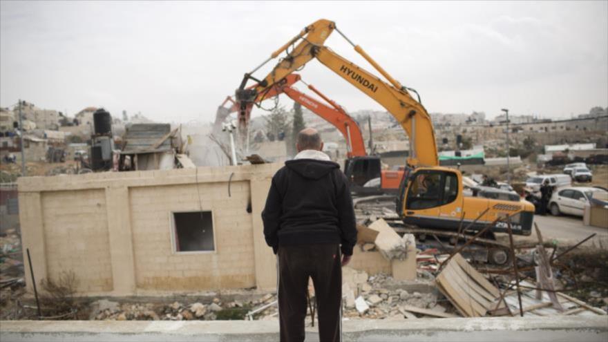 Un hombre palestino observa cómo fuerzas israelíes destruyen su casa.