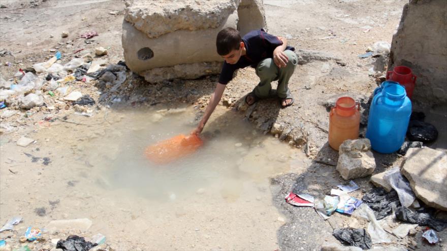 Un niño sirio está recogiendo agua contaminada de un pequeño estanque. 