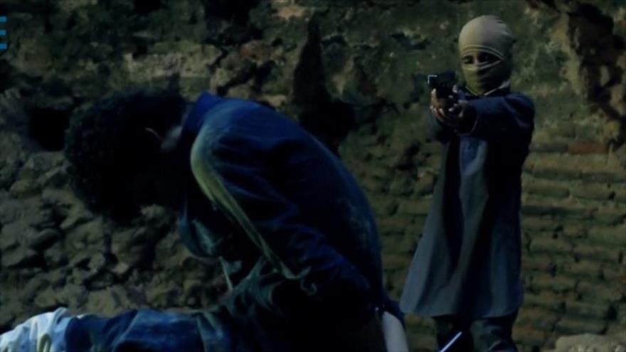 Un integrante menor de edad del grupo terrorista EIIL (Daesh, en árabe) ejecuta con una pistola a un preso sirio.
