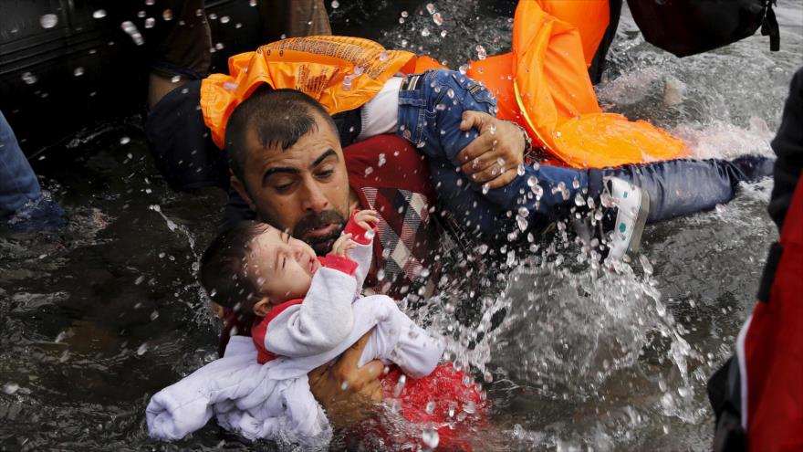 Un refugiado sirio se aferra a sus hijos para protegerlos de las olas de mar al llegar a la isla griega de Lesbos cruzando el mar de Egeo, 24 de septiembre de 2015. 