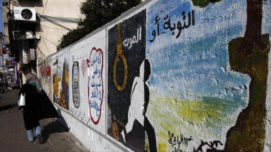Mujer palestina camina fretne a una pared en Gaza en la que se condena el espionaje para el régimen israelí.