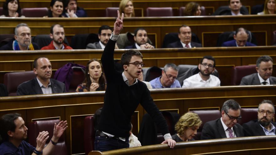 El diputado y secretario político de Podemos, Íñigo Errejón (de pie), muestra el signo de la victoria mientras que el líder de la formación, Pablo Iglesias (izda.) aplaude durante la constitución del Congreso. 13 de enero de 2016. 