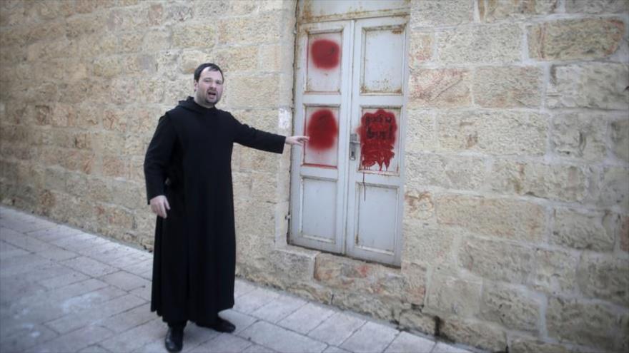 Un clérigo cristiano muestra las pintadas anticristianas hechas por colonos israelíes en el edificio de la Abadía de la Dormición en Al-Quds, 17 de enero de 2016.