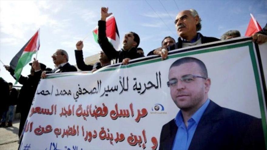 Manifestantes palestinos portan pancartas con la imagen del periodista preso en huelga de hambre, Mohamad al-Qiq.