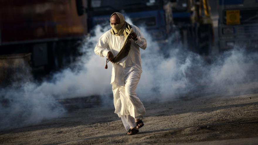 Hombre bareiní con el rostro cubierto huye de los gases lacrimógenos disparados por las fuerzas de seguridad en una manifestación antigubernamental en Sitra, al sur de capitalina Manama.