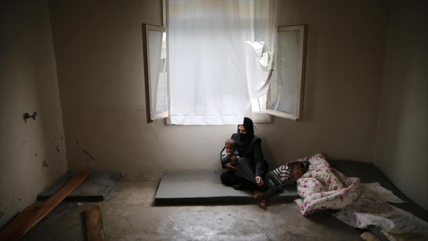 Una mujer refugiada siria con sus dos hijos en una casa en ruinas.