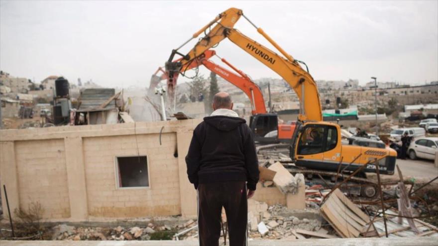 Un hombre palestino observa cómo las fuerzas del regimen israelí destruyen su casa.