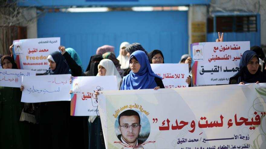 Mujeres palestinas portan pancartas en las que piden liberación del periodista palestino Mohamad al-Qiq.