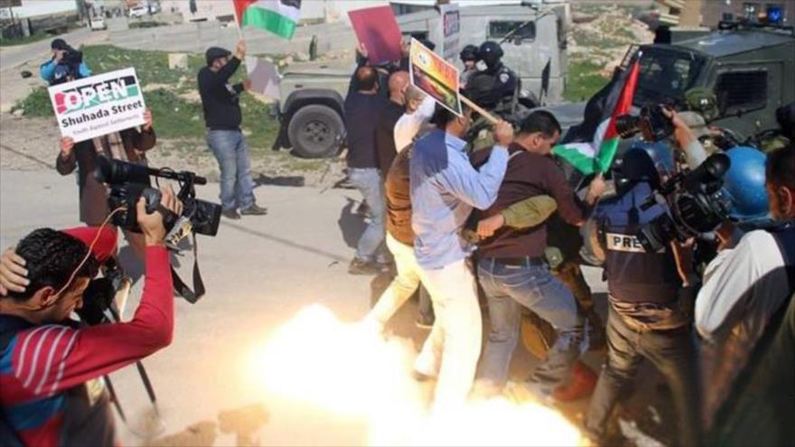 Los manifestantes y periodistas palestinos se dispersan tras el lanzamiento de una granada de aturdimiento por las fuerzas israelíes en Al-Jalil (Hebrón), 26 de febrero de 2016.