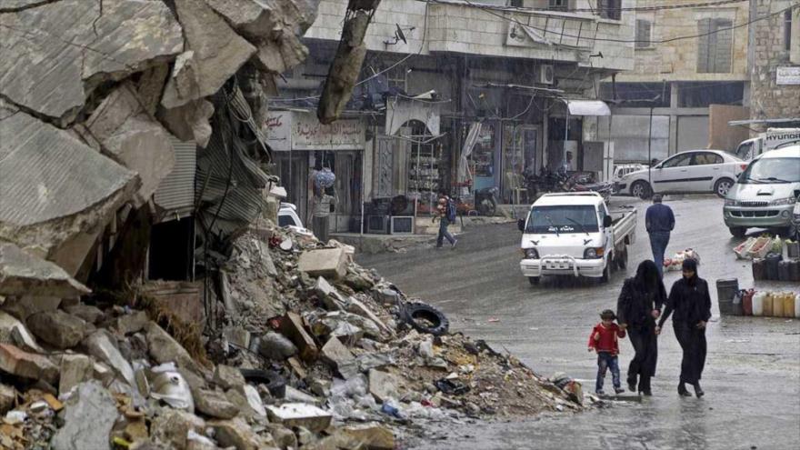Civiles caminan bajo la lluvia junto a un edificio destruido en el pueblo de Maaret al Numan, en Siria.