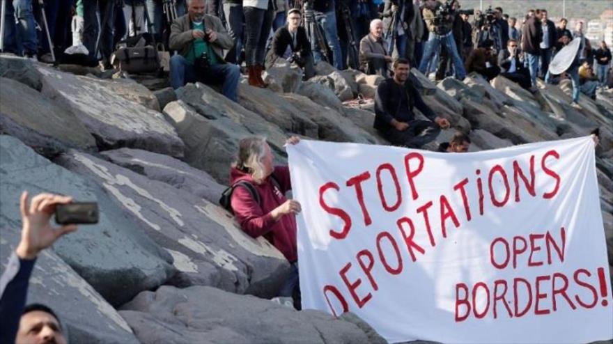 Activistas sostienen pancartas mientras llegan refugiados al puerto de Dikili en Izmir (Turquía) provenientes de la isla de Lesbos. 