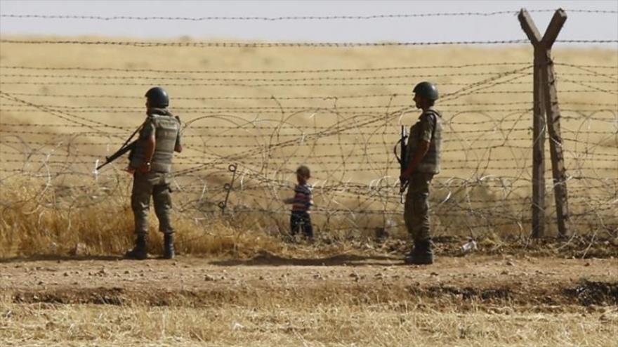 Soldados turcos y un niño sirio en la frontera turco-siria.