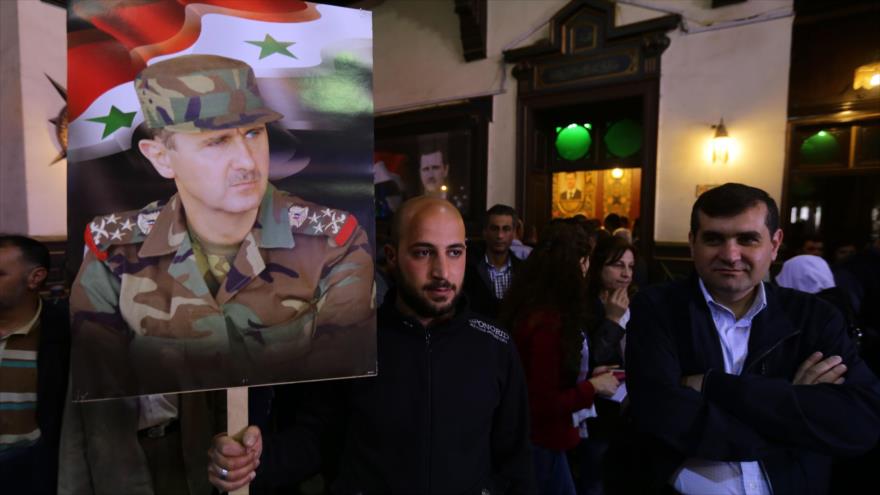 Sirios presentes en un colegio electoral en la capitalina ciudad de Damasco llevan retrato del presidente Bashar al-Asad, 13 de abril de 2016.