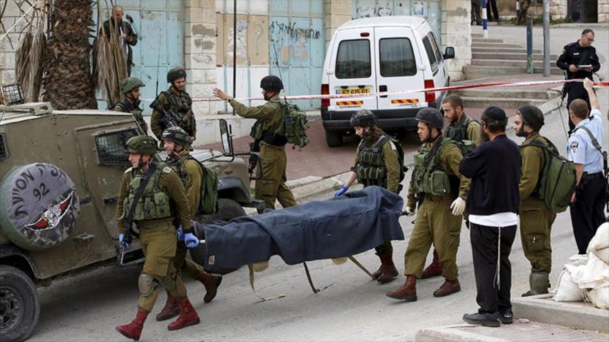 Soldados israelíes trasladan el cuerpo del jóven palestino, que murió por los ataques de las tropas del regimen israelí en el barrio de Al-Jalil (Hebrón), 24 de marzo de 2016.