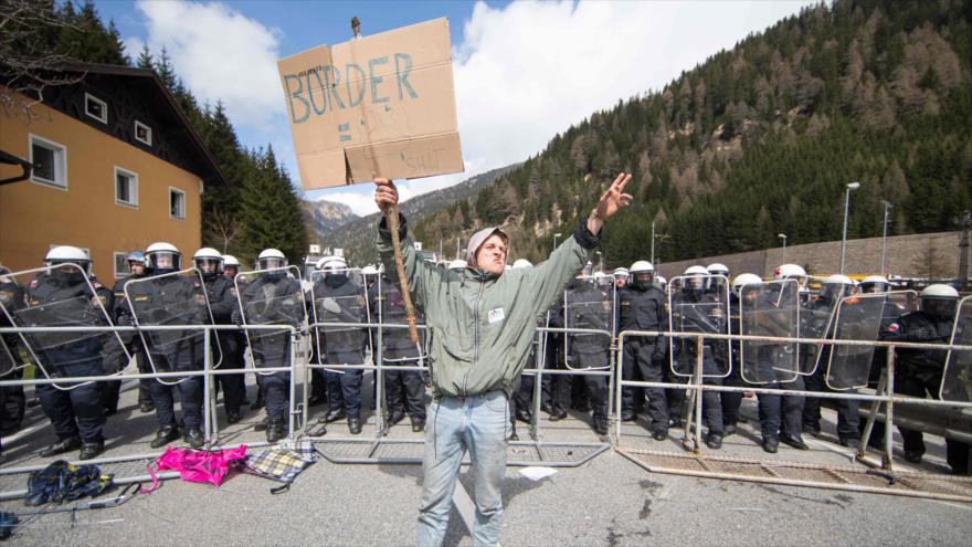 Un manifestante prorrefugiados exhibe una pancarta ante la policía en el puerto de montaña austriaco-italiano de Brenner, en protesta por la próxima imposición de controles fronterizos, 24 de abril de 2016.