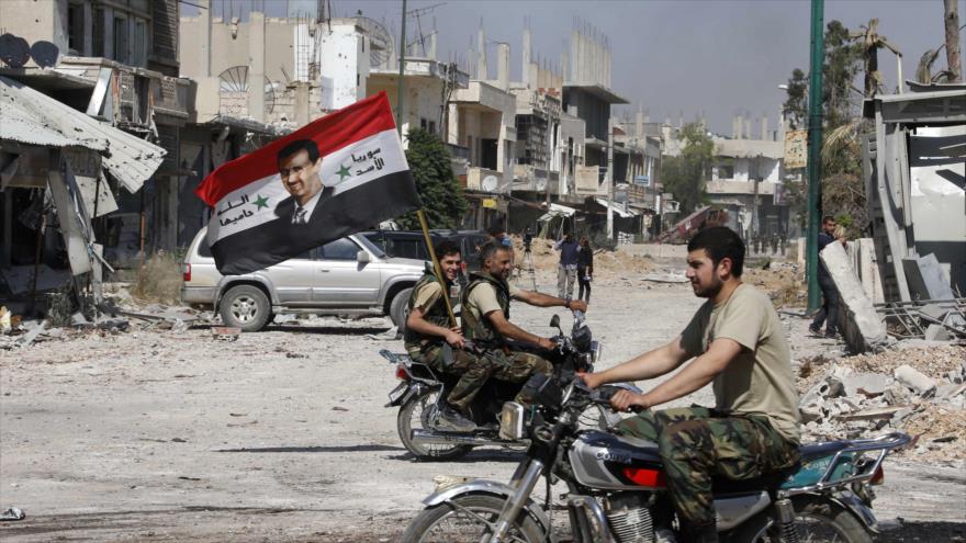 Soldados sirios patrullan las calles de una zona en Homs, portando una bandera nacional con la imagen del presidente de Siria, Bashar al-Asad.