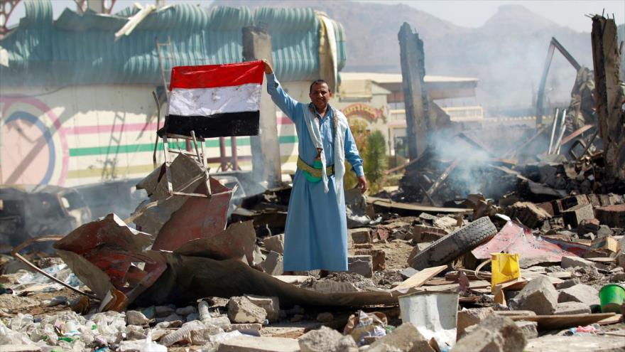 Un yemení sostiene su bandera nacional entre las ruinas de una escuela destruida por un ataque aéreo de Arabia Saudí a la capital Saná, 12 de febrero de 2016.