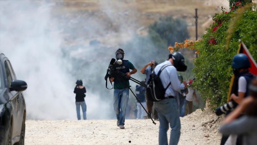 Periodistas trabajan en medio del humo dejado por los gases lacrimógenos durante los enfrentamientos entre palestinos y militares israelíes israelíes en el pueblo cisjordano de Bilin, cerca de Ramalá, 13 de mayo de 2016.