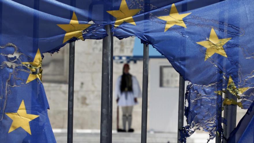 Un guardia presidencial griego visto por el agujero de una bandera de la Unión Europea medio quemada por los manifestantes en Atenas.
