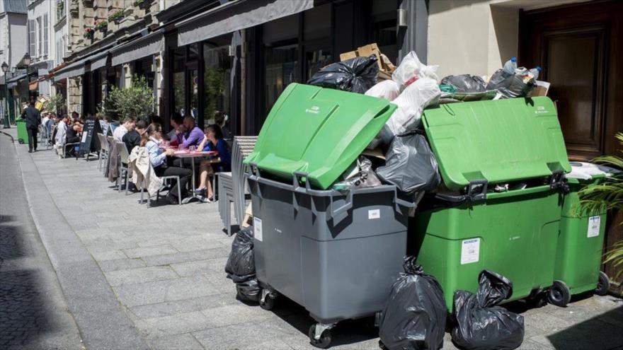 Gente comiendo junto a bolsas de basura amontonadas en París, capital Francia, por la huelga de recolectores de basura, 9 de junio de 2016. 
