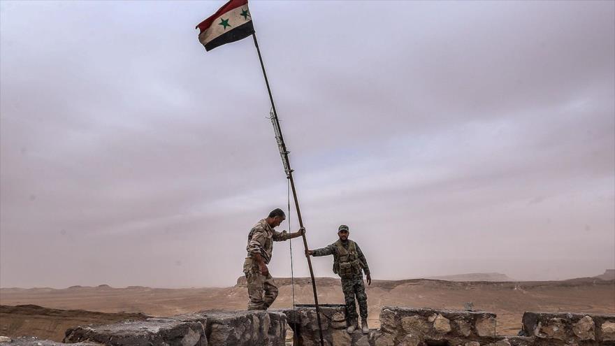 Soldados sirios alzan la bandera de su país.