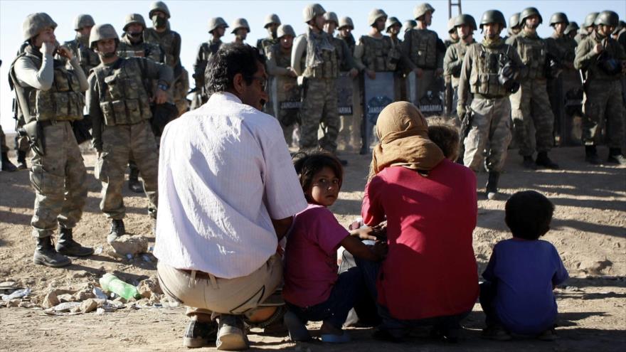 Una familia siria espera ante soldados turcos el permiso de entrada en la ciudad turca de Sanliurfa.