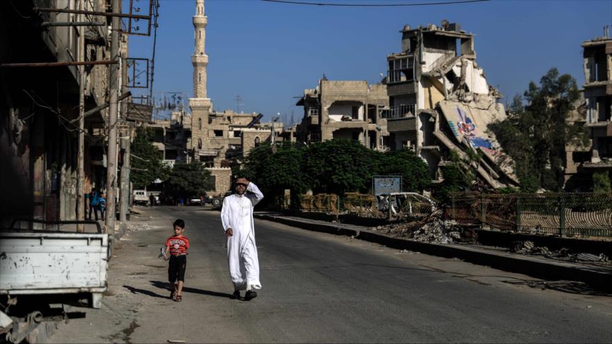 Un hombre y un niño caminan por las calles de un destrozado barrio cerca de Damasco, Siria.