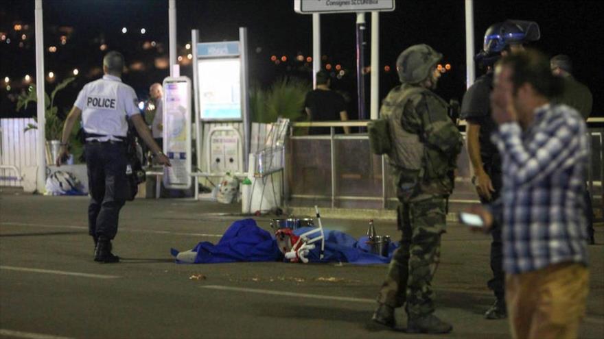 Soldados, agentes de policía y bomberos a pie cerca del cadáver de una persona cubierto con sábanas de color azul en el paseo marítimo Promenade des Anglais, en la ciudad francesa de Niza, donde un camión embistió a una multitud, 15 de julio de 2016.