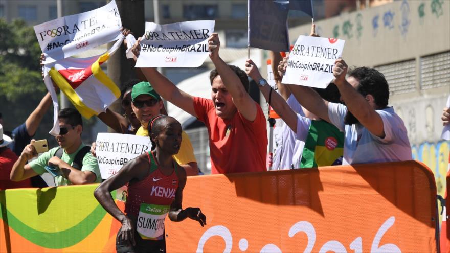 Brasileños protestan con pancartas "Fora Temer" durante el desarrollo de la maratón femenina de Río 2016 al paso de la atleta keniana Jemima Jelagat Sumgong, 14 de agosto 2016.