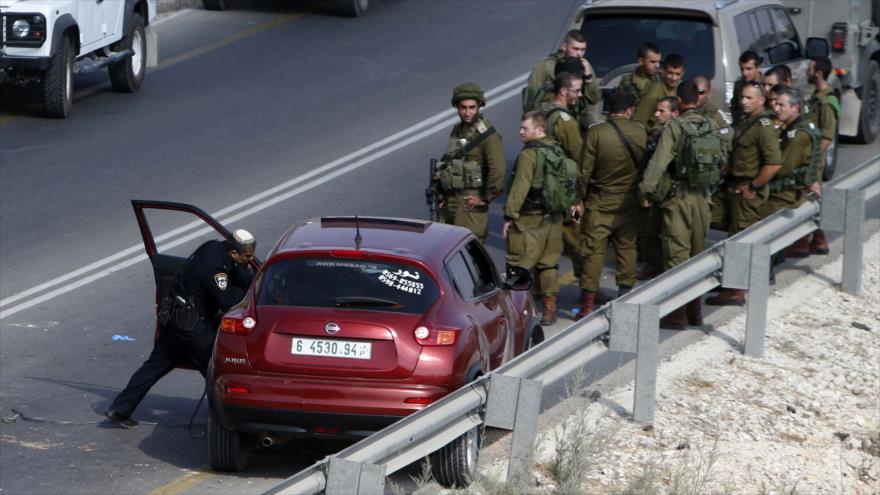 Un policía del régimen israelí investiga el coche en el que era un palestino que murió a tiros por las fuerzas israelíes en la ciudad cisjordana de Nablus, 24 de agosto de 2016.