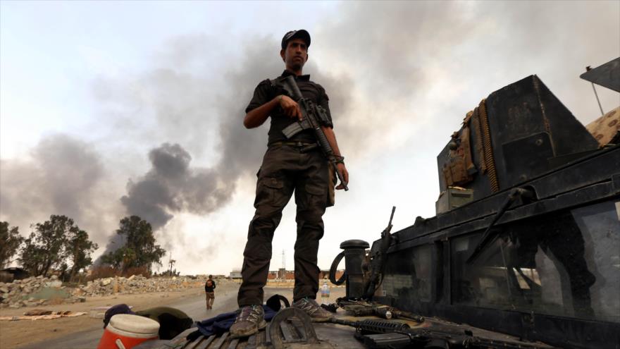 Un soldado iraquí posa sobre un vehículo militar, mientras que en el fondo se ve humo negro de un incendio provocado por Daesh en un yacimiento petrolífero en la ciudad de Al-Qayara antes de huir de la zona, 30 de agosto de 2016.