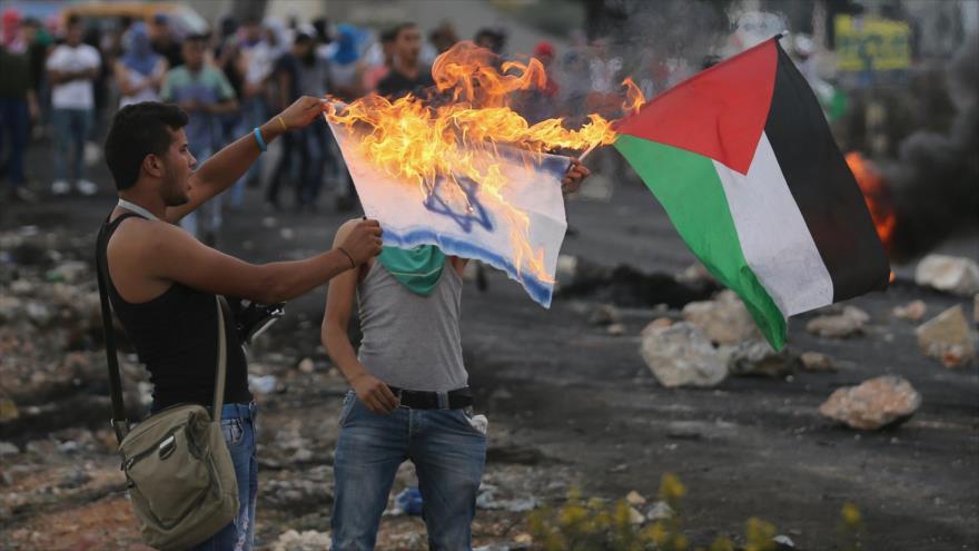 Un manifestante palestino quema bandera israelí durante los enfrentamientos con las fuerzas israelíes cerca de la ciudad cisjordana de Ramalá, 18 de octubre de 2015.