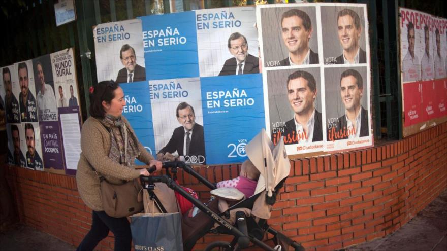 Una mujer pasea delante de una pared con carteles electorales de algunos de los candidatos de los distintos partidos, de cara a los comicios generales españoles del 20 de diciembre de 2015.
