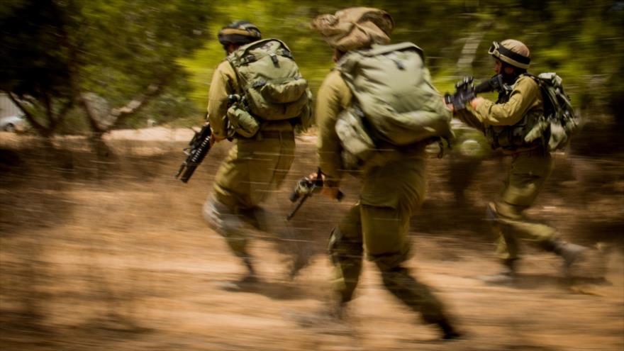 Tres soldados israelíes corren con sus armas automáticas durante un ataque del régimen a la Franja de Gaza, 4 de agosto de 2014.